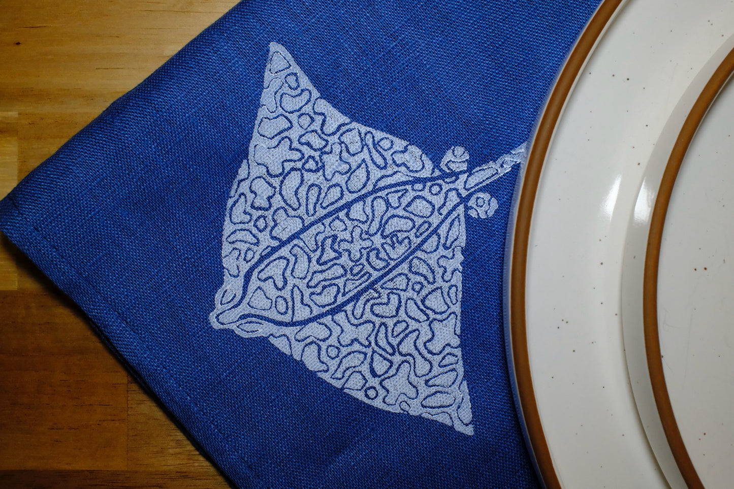 &BEYOND Eagle Ray Blues linen napkins displayed folded on a dining table.
