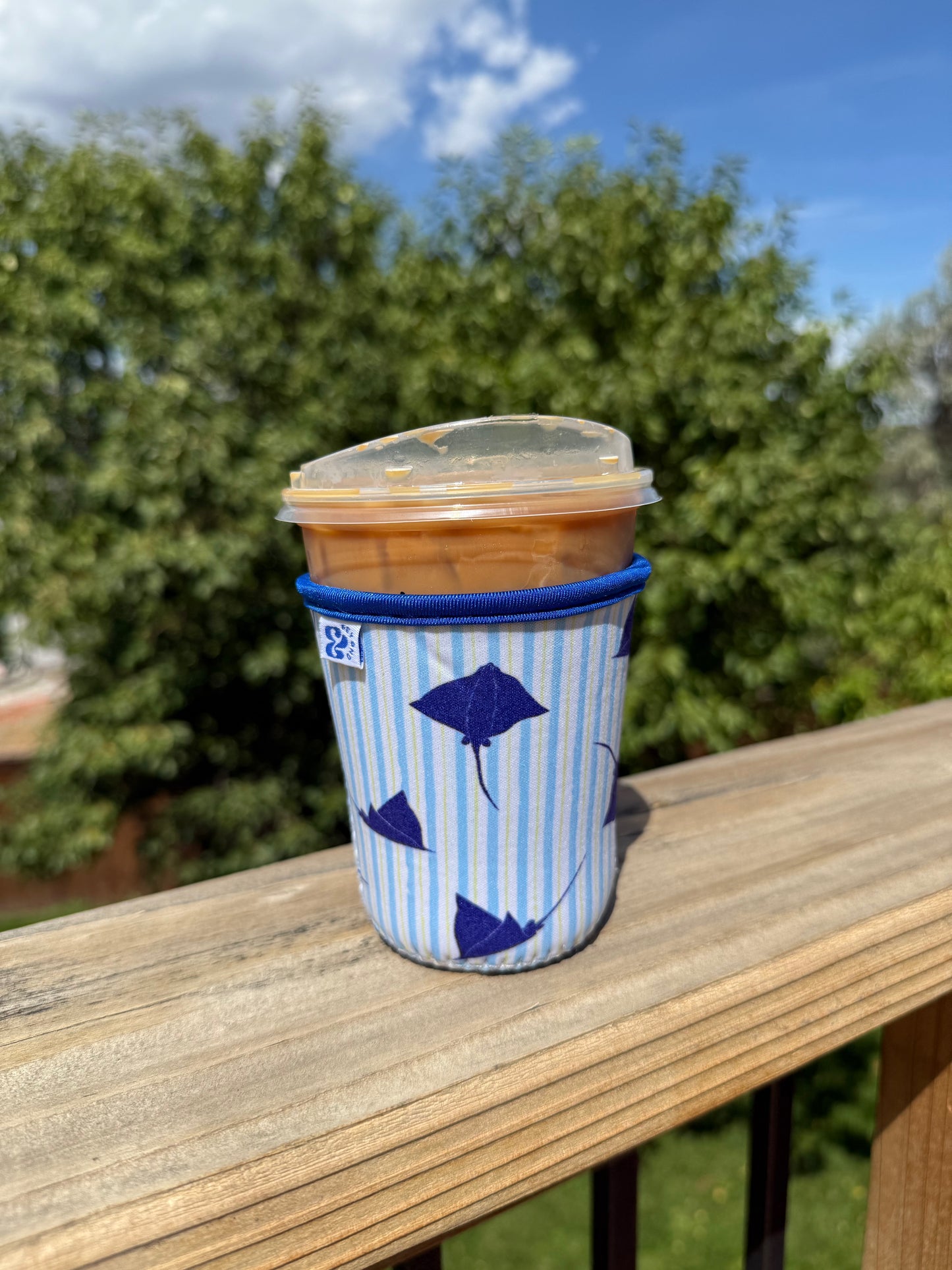 &BEYOND Eagle Ray iced coffee coozie featured outdoors on a patio table.