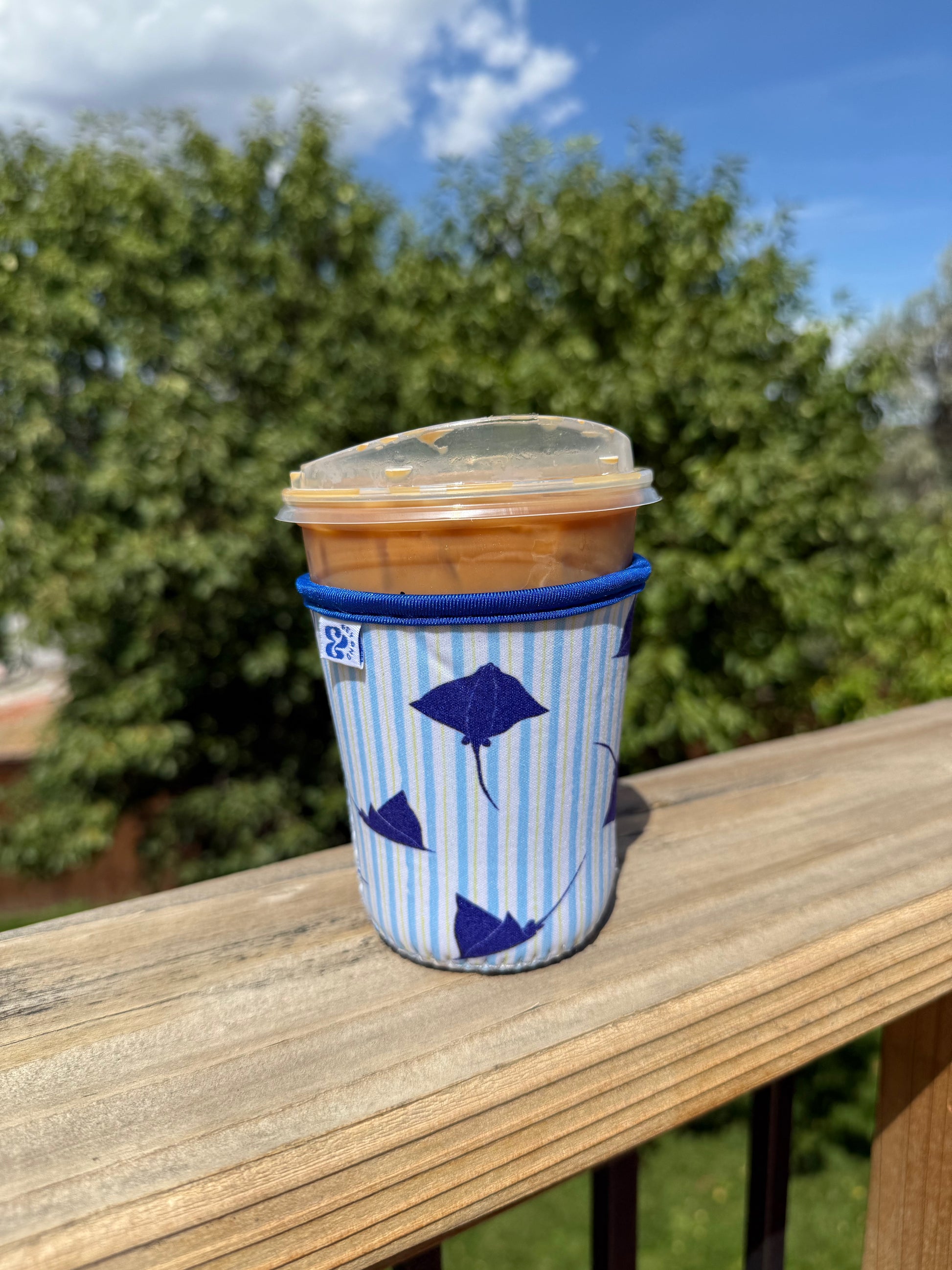 &BEYOND Eagle Ray iced coffee coozie featured outdoors on a patio table.