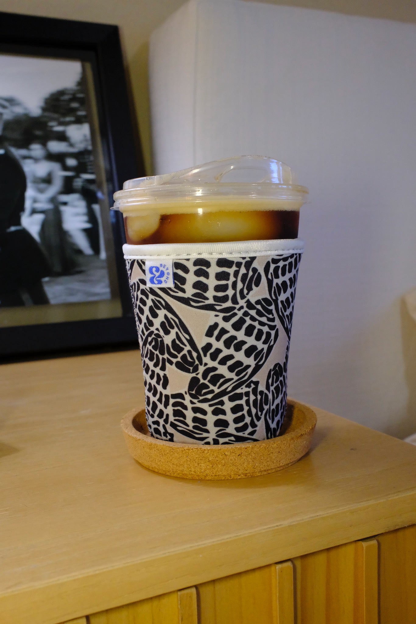 Lifestyle photo of the &BEYOND Hebrew Shell coozie on a wooden surface.